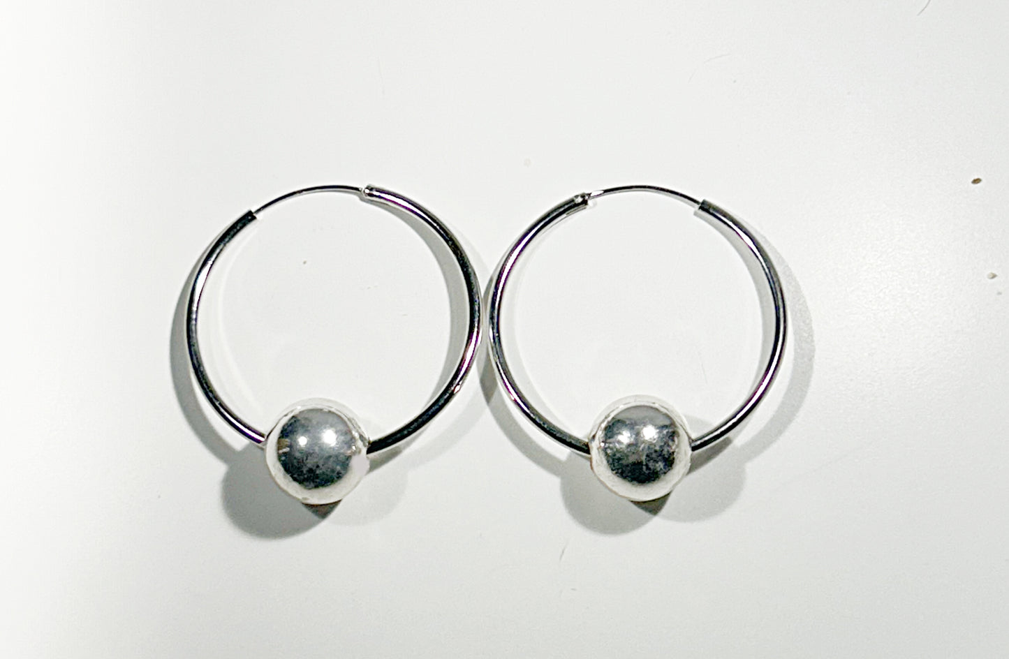 Pair of silver hoop earrings with round floating ball on a white background