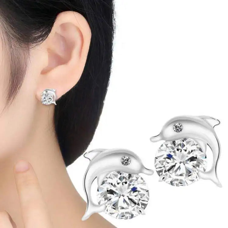 Silver dolphin stud earrings with large clear round gemstones, shown worn on a model's ear and displayed separately on a white background.