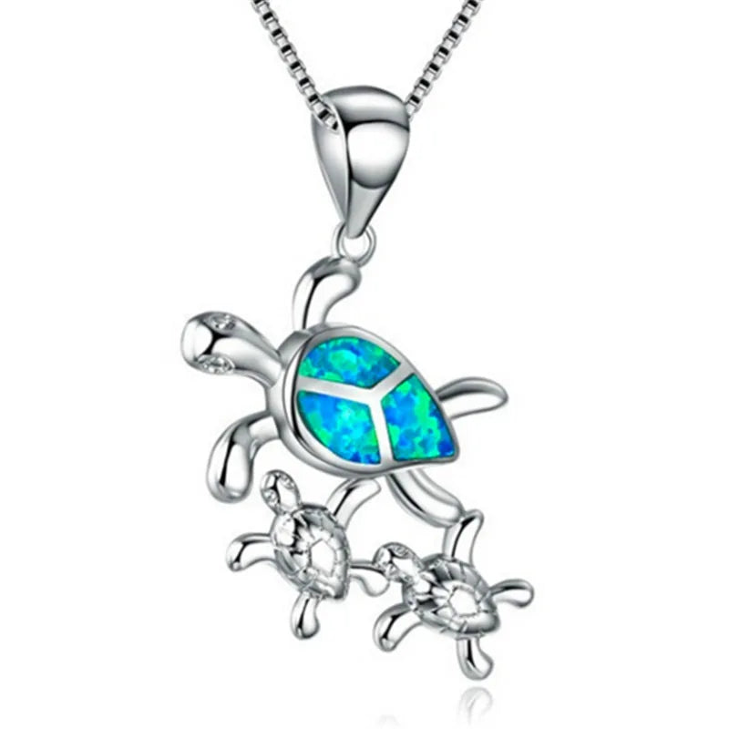A silver pendant necklace featuring a mother sea turtle with a vibrant blue and green opal inlay, accompanied by two small silver sea turtles, suspended from a silver box chain against a white background.