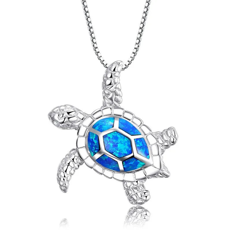 A silver turtle pendant necklace featuring a vibrant blue opal inlay on the shell, suspended from a silver ball chain against a white background.