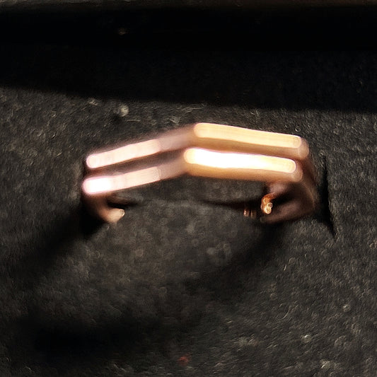 A minimalist double-bar ring in a warm gold or rose-gold metal, displayed on a textured black surface.