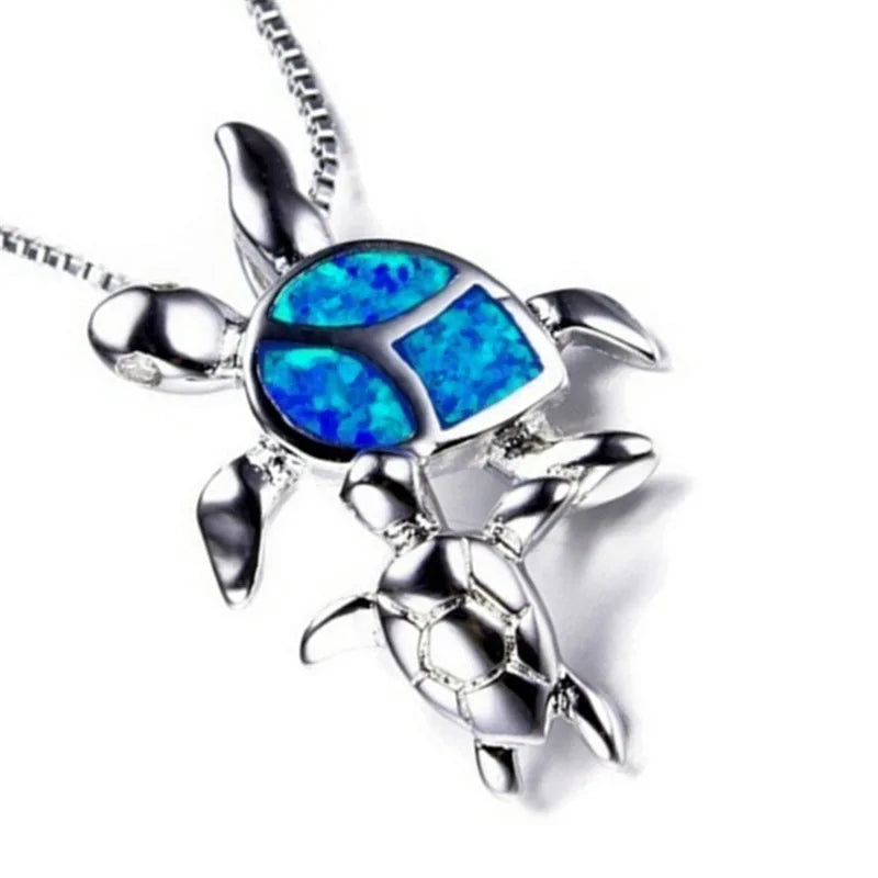 A silver-toned turtle pendant necklace featuring a vibrant blue inlay resembling opal on the shell, shown on a white background.