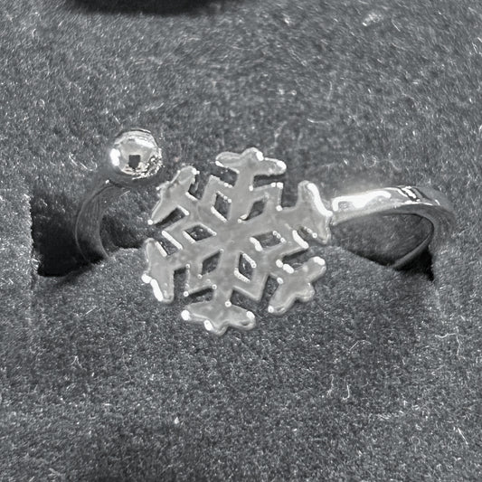 A silver snowflake-shaped ring with a small clear crystal bead on the band, displayed in a textured black velvet ring box.