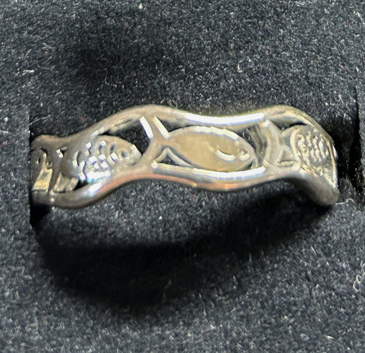 A silver ring featuring a stylized fish design with textured scales, photographed on a black textured velvet surface.