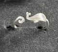 A pair of silver whale-shaped rings displayed on a dark textured velvet ring box.