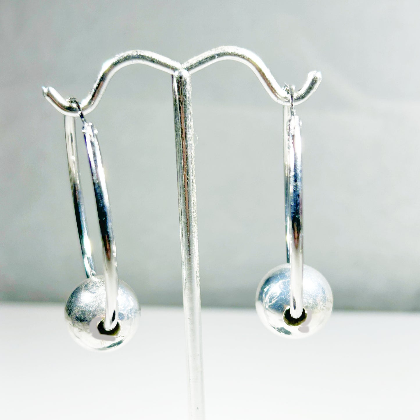 Silver earrings with floating round ball 
on a stand with a plain background