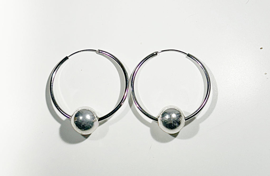 Pair of silver hoop earrings with round floating ball on a white background