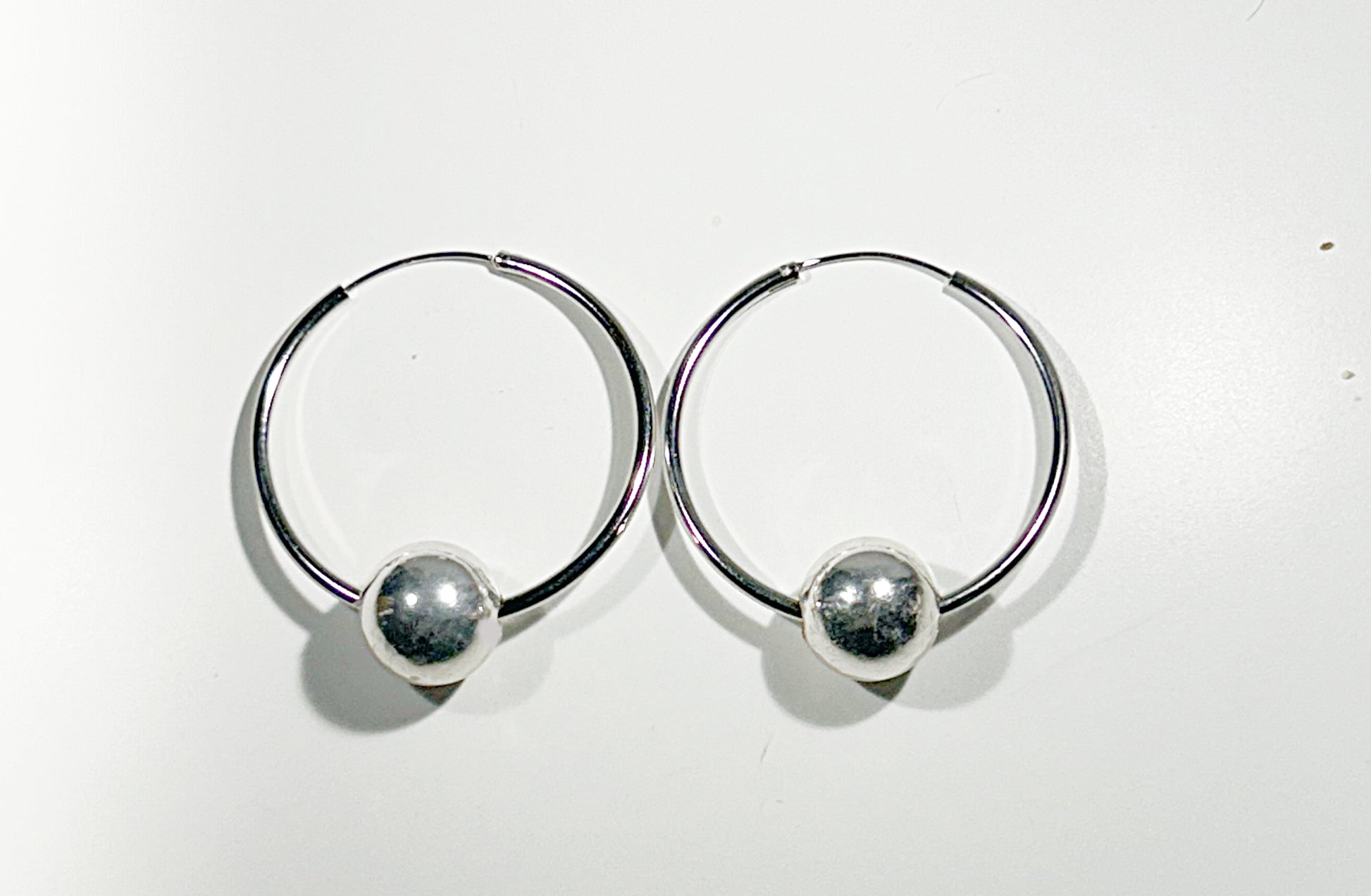 Pair of silver hoop earrings with round floating ball on a white background