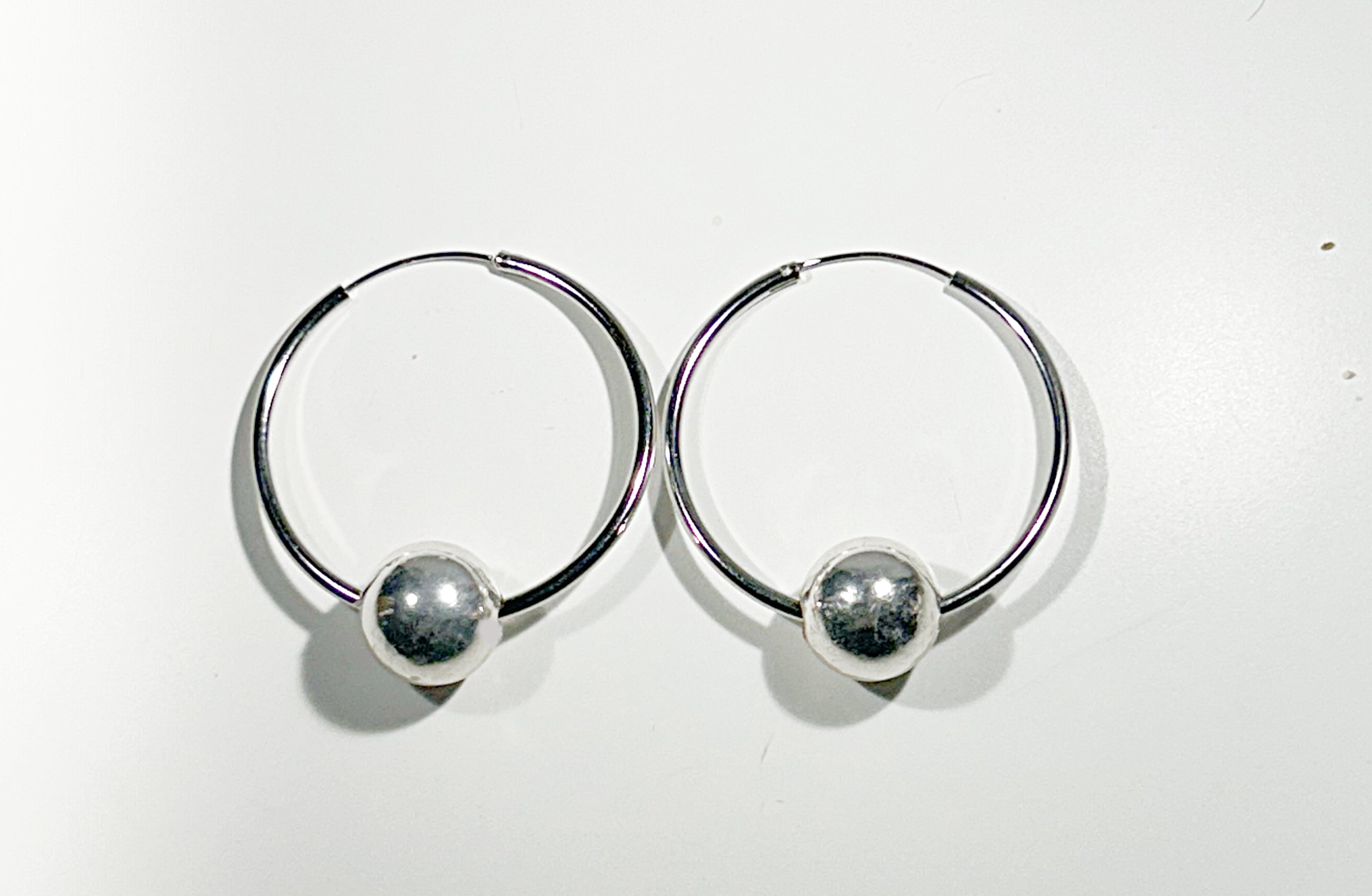 Pair of silver hoop earrings with round floating ball on a white background