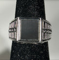 A silver-toned signet ring with a rectangular face and decorative beaded side bands, displayed on a black velvet ring stand against a light gray background.