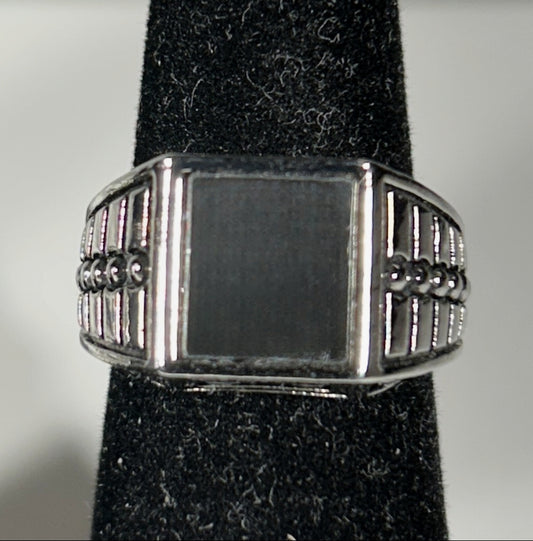 A silver-toned signet ring with a rectangular face and decorative beaded side bands, displayed on a black velvet ring stand against a light gray background.