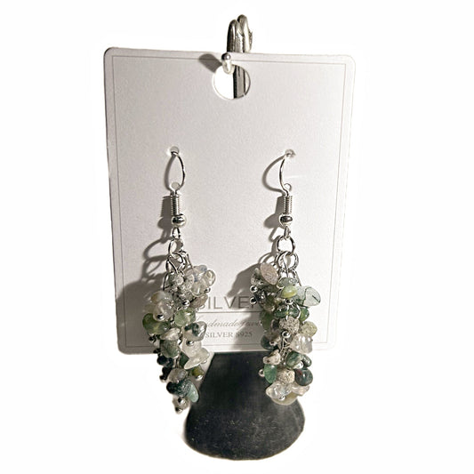 A pair of dangling earrings with clusters of clear and pale green faceted beads on silver hooks, displayed on a white card against a white background.