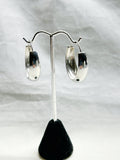 Silver hoop earrings on a black stand against a white background
