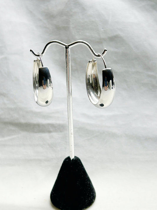 Silver hoop earrings on a black stand against a white background