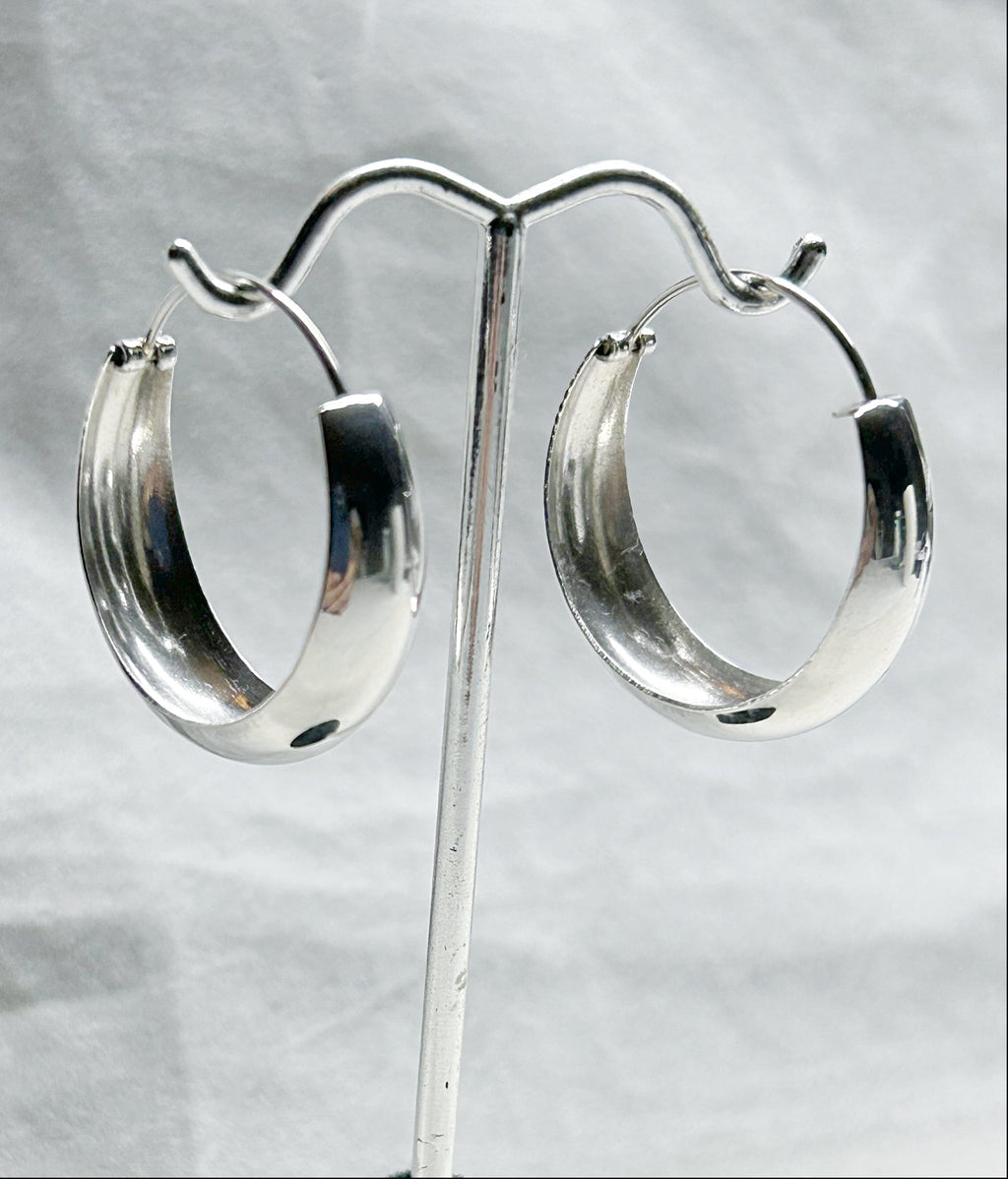 Silver hoop earrings on a stand against a light gray background