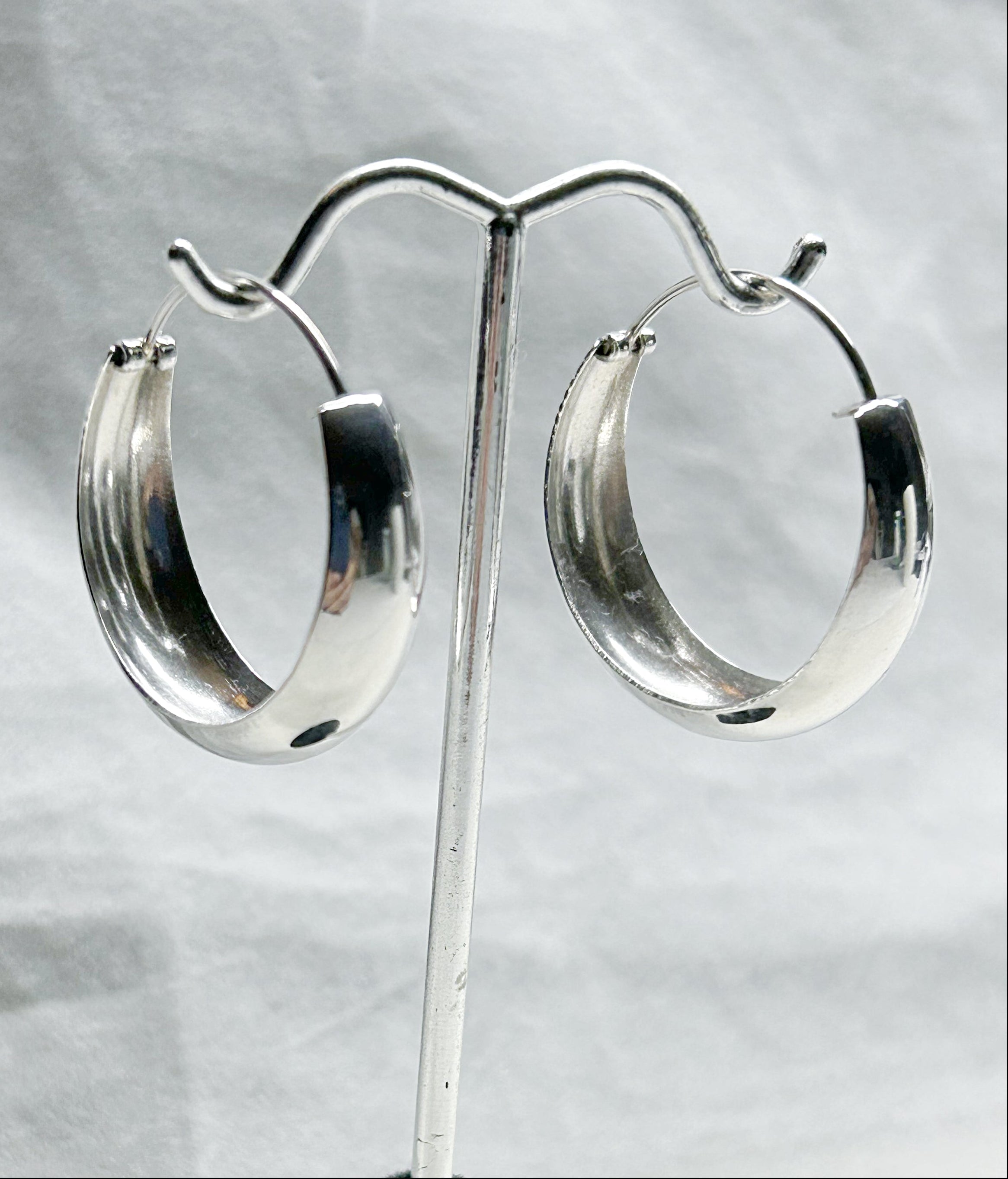 Silver hoop earrings on a stand against a light gray background