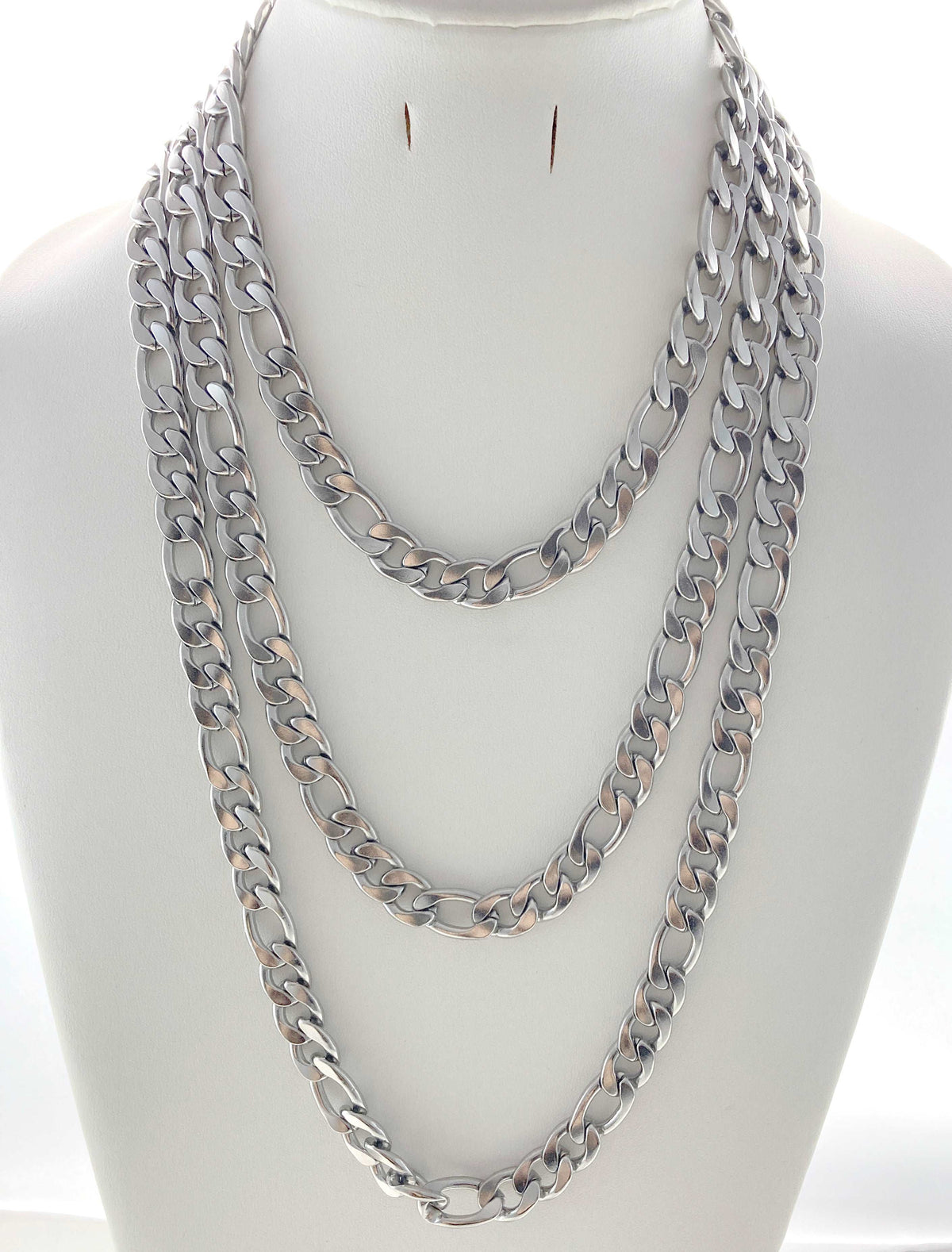 Three layered silver-tone Cuban link chain necklaces displayed on a white mannequin bust against a white background.