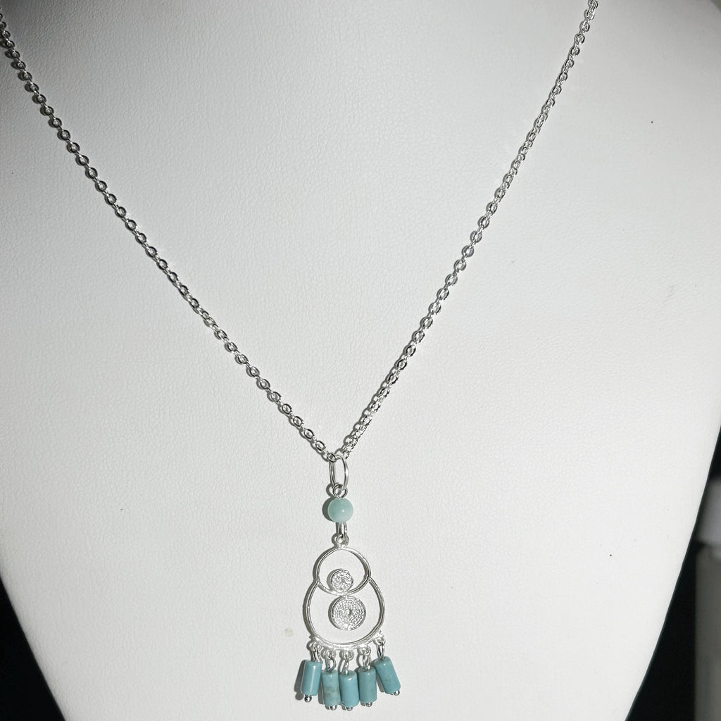 Necklace with a silver pendant and turquoise beads on a white mannequin.