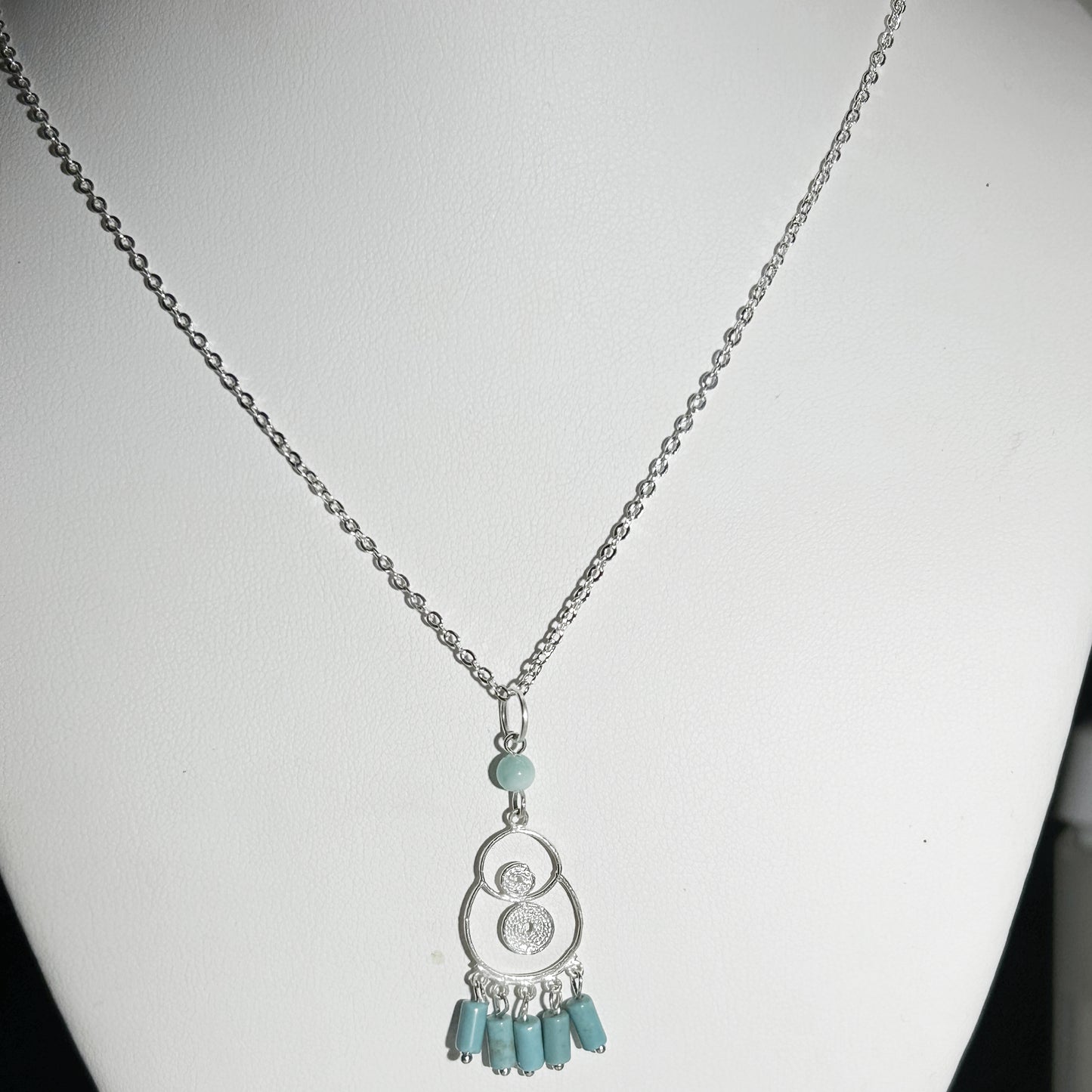 Necklace with a silver pendant and turquoise beads on a white mannequin.