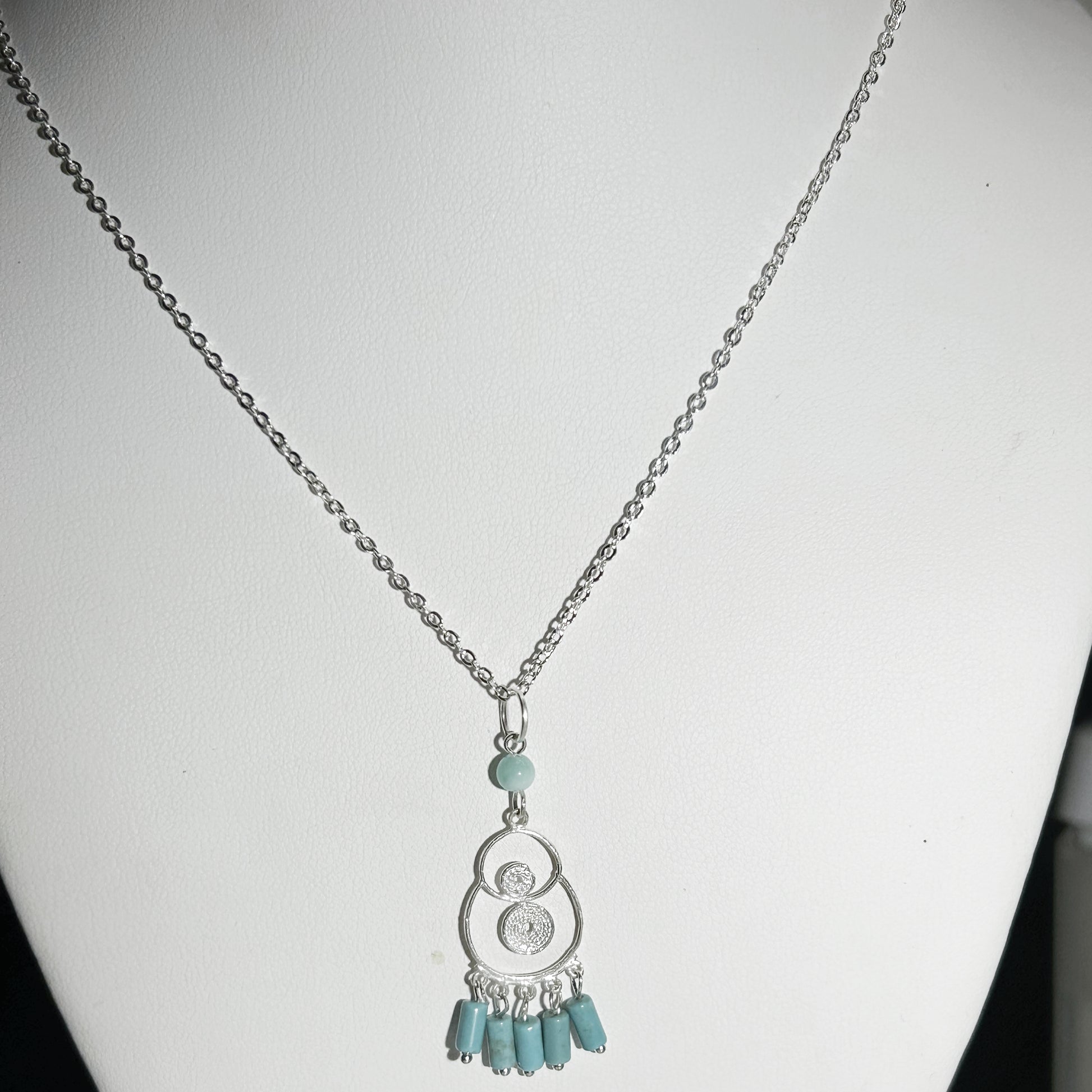 Necklace with a silver pendant and turquoise beads on a white mannequin.