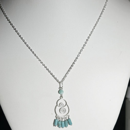 Necklace with a silver pendant and turquoise beads on a white mannequin.