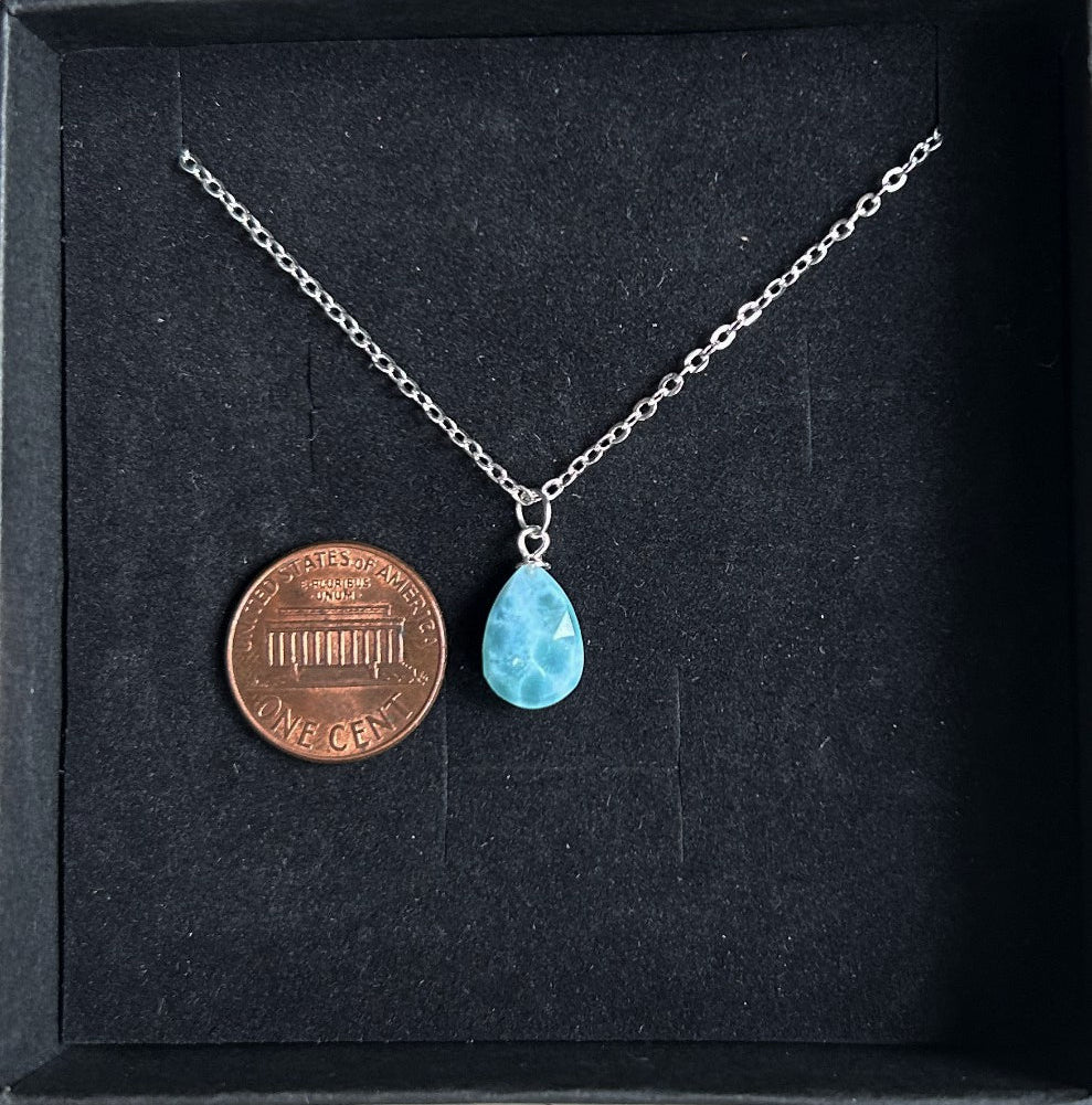 Necklace with a blue teardrop pendant next to a penny on a black background