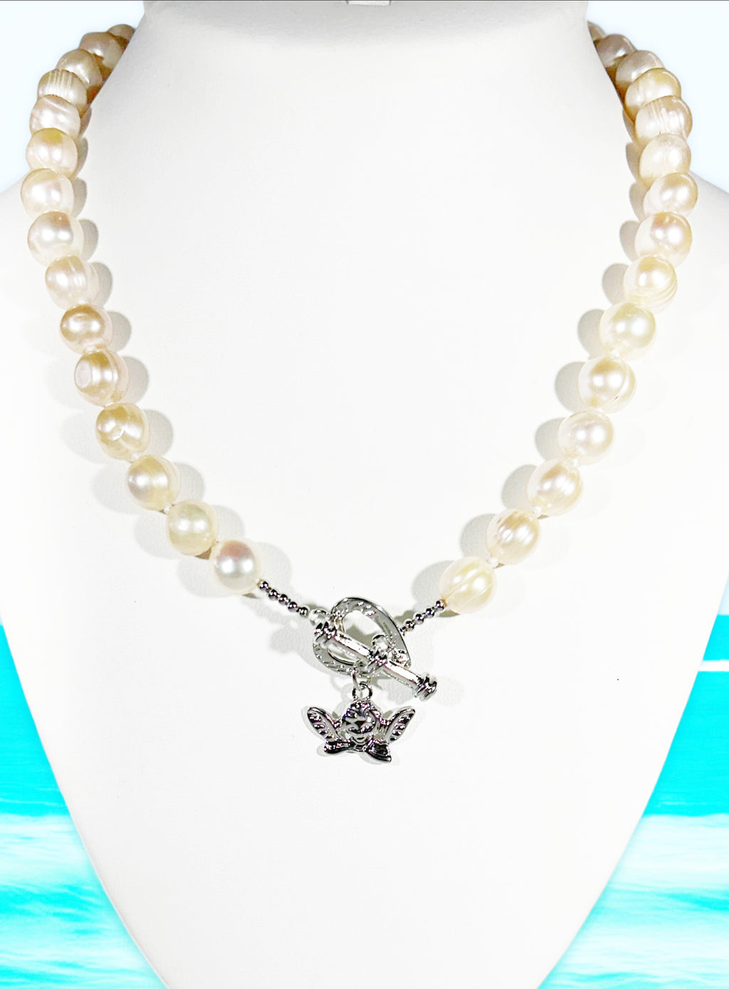 Pearl necklace with a silver butterfly charm on a white mannequin against a blue and green abstract background.