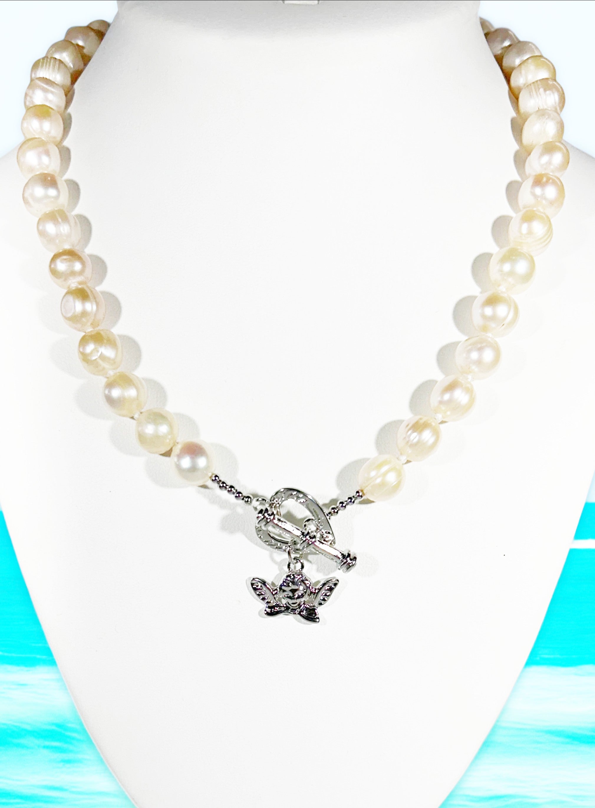 Pearl necklace with a silver butterfly charm on a white mannequin against a blue and green abstract background.